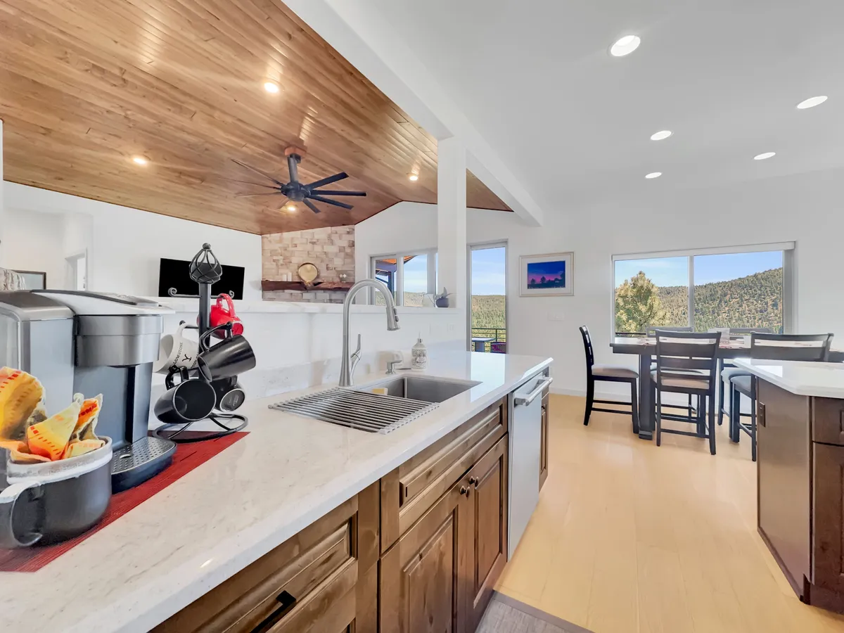 A bright, modern kitchen with a central island, coffee maker, dining table, and large windows flooding the space with natural light. It's designed for cooking, entertaining, and enjoying meals with loved ones while surrounded by mountain views.