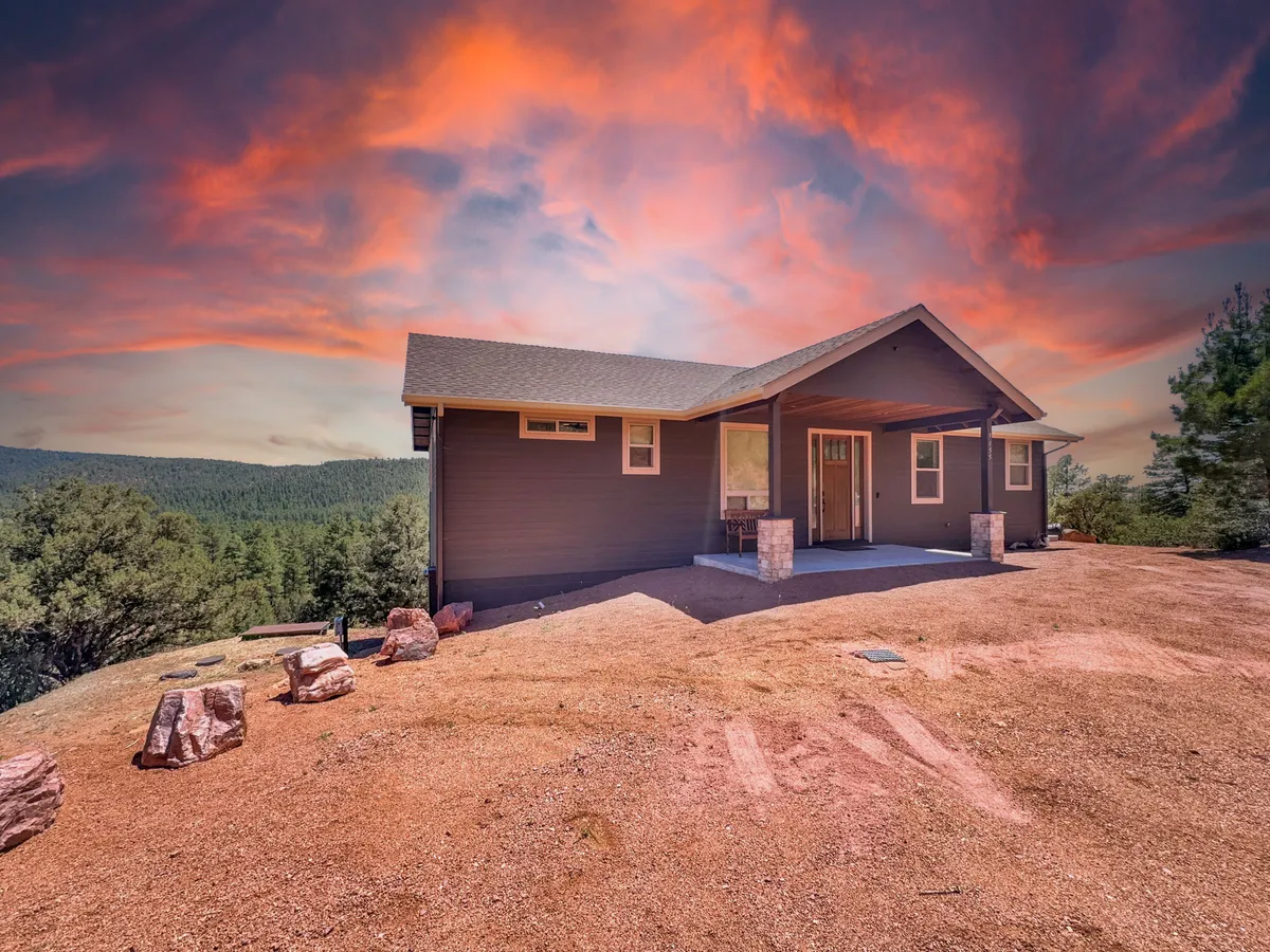 This image presents the house’s inviting facade, featuring a wraparound porch with comfortable seating and a mountain backdrop under a vibrant sky. The view hints at both forest trails and the relaxing possibilities on the porch, blending adventure and tranquility.
