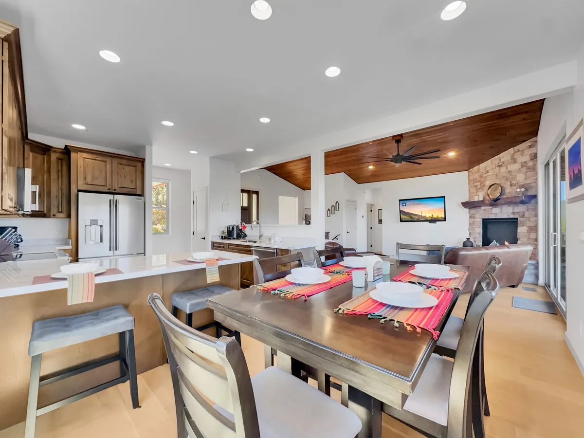 An inviting open-concept area that includes a stylish dining table with a colorful setting, a kitchen with warm wooden cabinetry, and a living area anchored by a stone fireplace. The space feels festive, ready for family meals or celebrating special occasions.