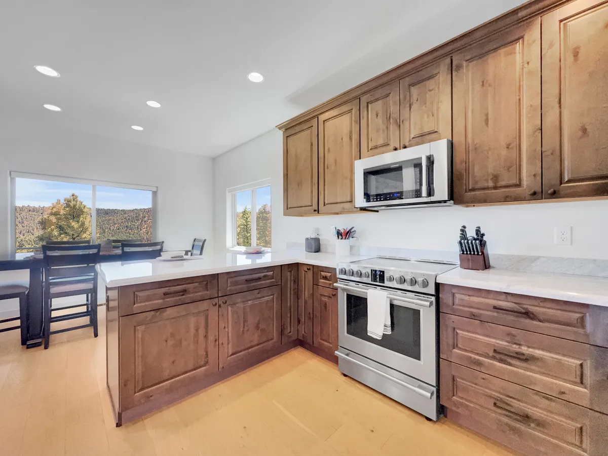 A modern kitchen with a central island, stainless steel appliances, ample wood cabinetry, and a large window offering a peaceful view. The kitchen is clearly set up for both cooking and socializing, with the island inviting casual conversation and lingering morning coffees.