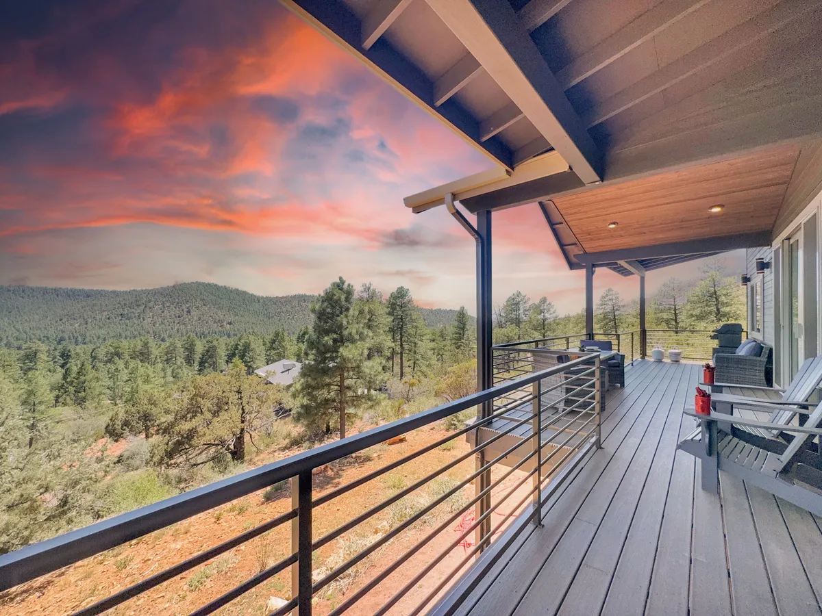 A wooden deck furnished with comfortable chairs offers a sweeping view of the mountains, framed by a glowing sunset sky. The deck's railing provides a sense of safety and openness, inviting guests to relax outdoors and take in the natural beauty. The scene conveys the peaceful transition from adventure to relaxation, with the deck acting as a perfect vantage point for soaking in the landscape.