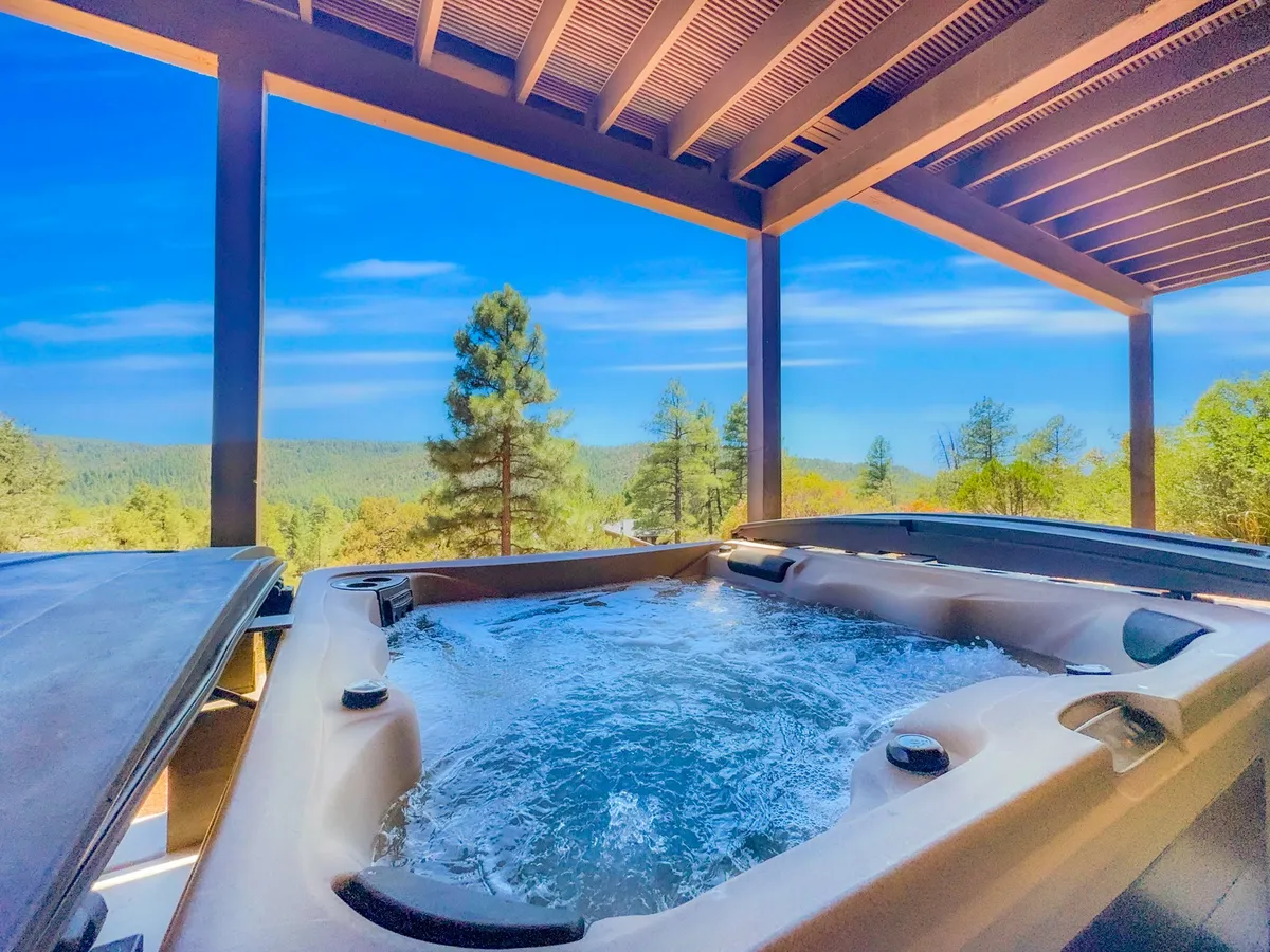 A steaming hot tub sits on a covered patio, overlooking lush forest and distant mountain peaks. Wooden beams frame the view, while the tranquil outdoor setting invites relaxation and rejuvenation. The inviting water and scenic backdrop make this an ideal spot for unwinding after active pursuits.