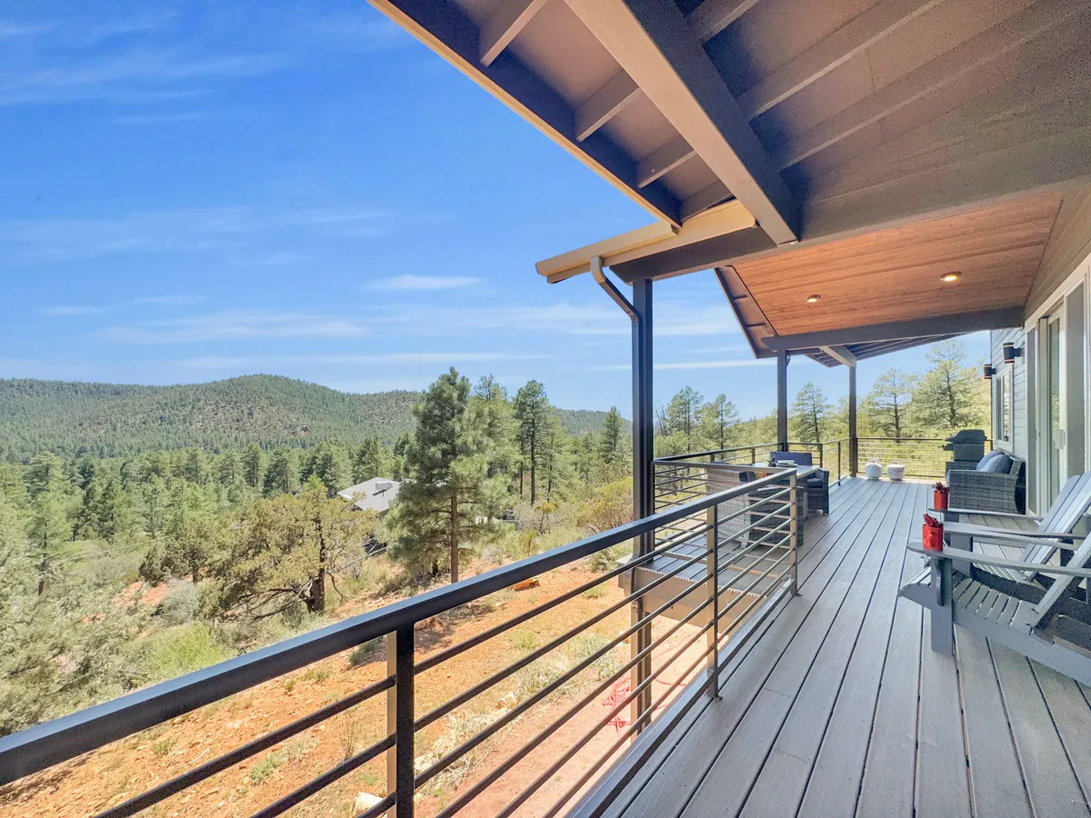 A spacious deck with wooden railings, comfortable outdoor seating, and a panoramic mountain view. The tranquil atmosphere is perfect for lounging with a book or sharing coffee, and the elevated perspective reinforces the 'among the treetops' narrative.