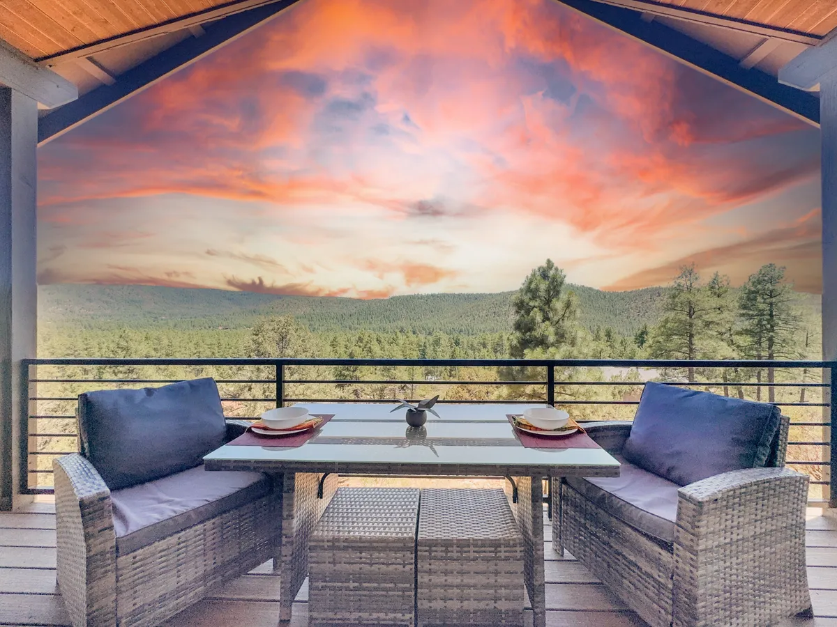 This image showcases an outdoor seating and dining area set against a backdrop of rolling hills and a colorful sunset. The table is ready for a meal, inviting couples to dine outside while soaking in the forested landscape and sunset ambiance.