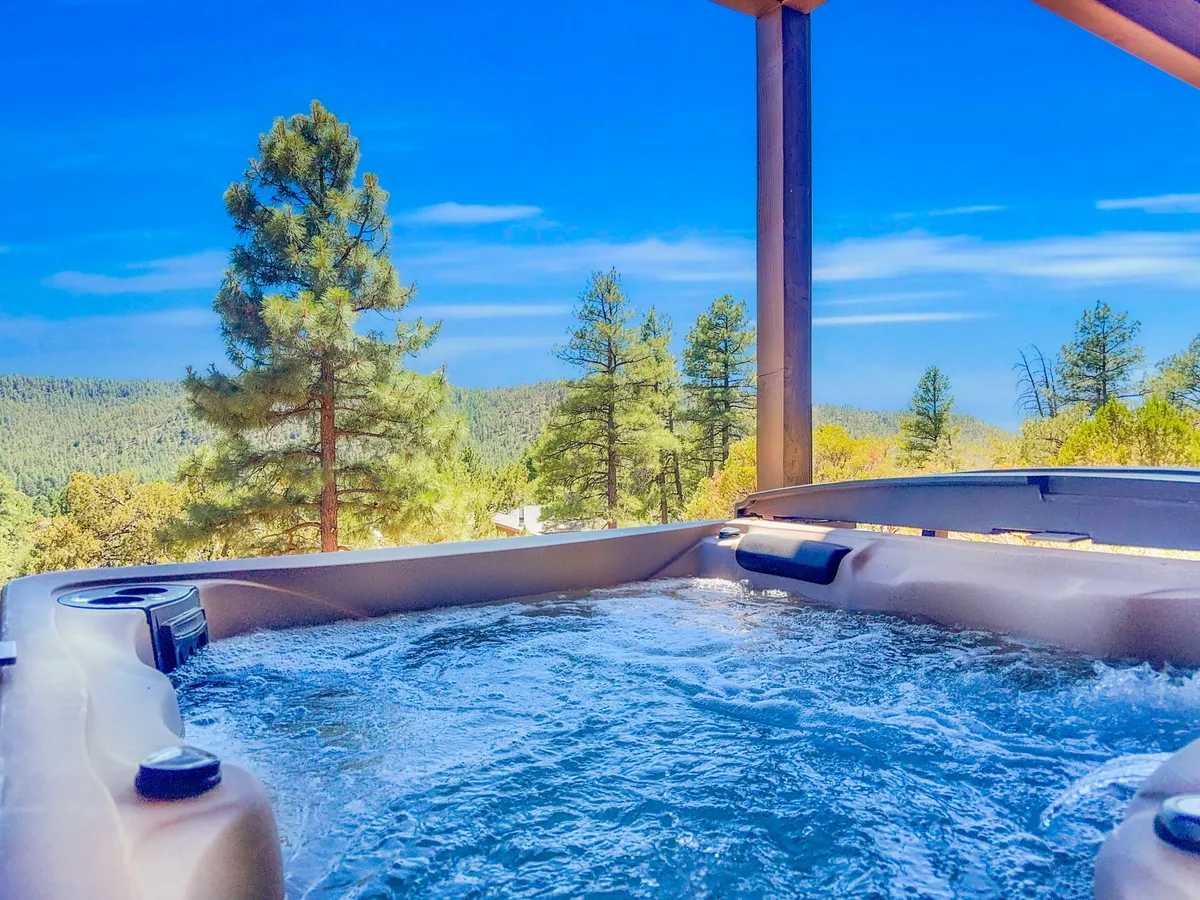 A serene hot tub nestled among tall pines, with mountain views visible beyond the deck. The scene suggests peaceful relaxation, perfect for stargazing or enjoying a soak as the sun sets.